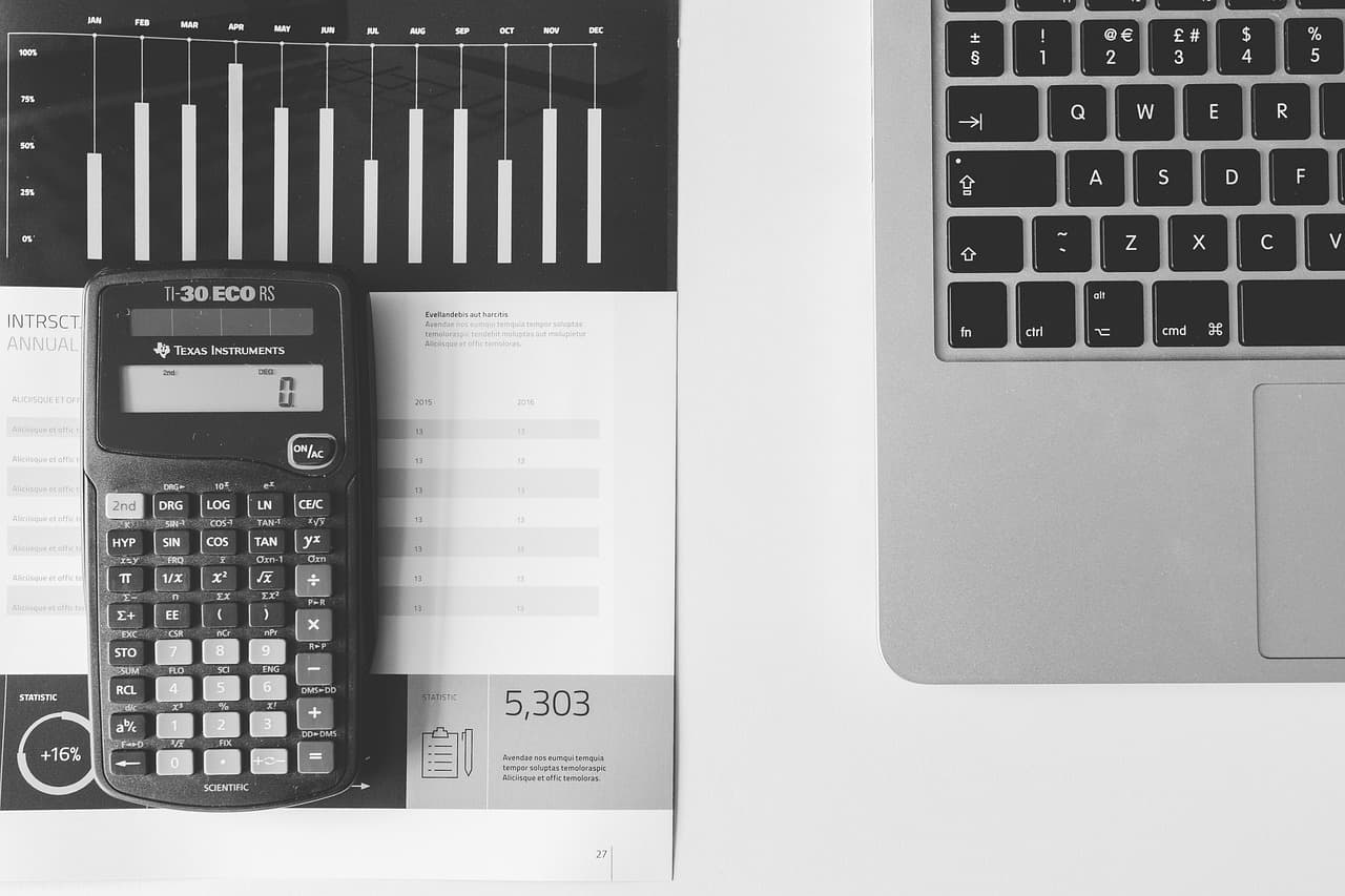 Um relatório impresso com um gráfico de barras e uma tabela de números, com uma calculadora científica pousada em cima, ao lado do teclado de um portátil